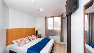 Ett hotellrum med en säng, en tv som är monterad på väggen, ett fönster med gardiner och en dörr.