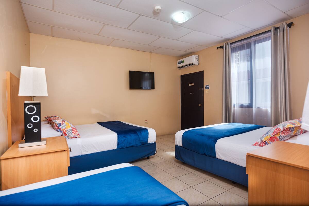 Ein Hotelzimmer mit zwei Betten, einem Fernseher, einer Klimaanlage und einem Fenster mit Vorhängen.
