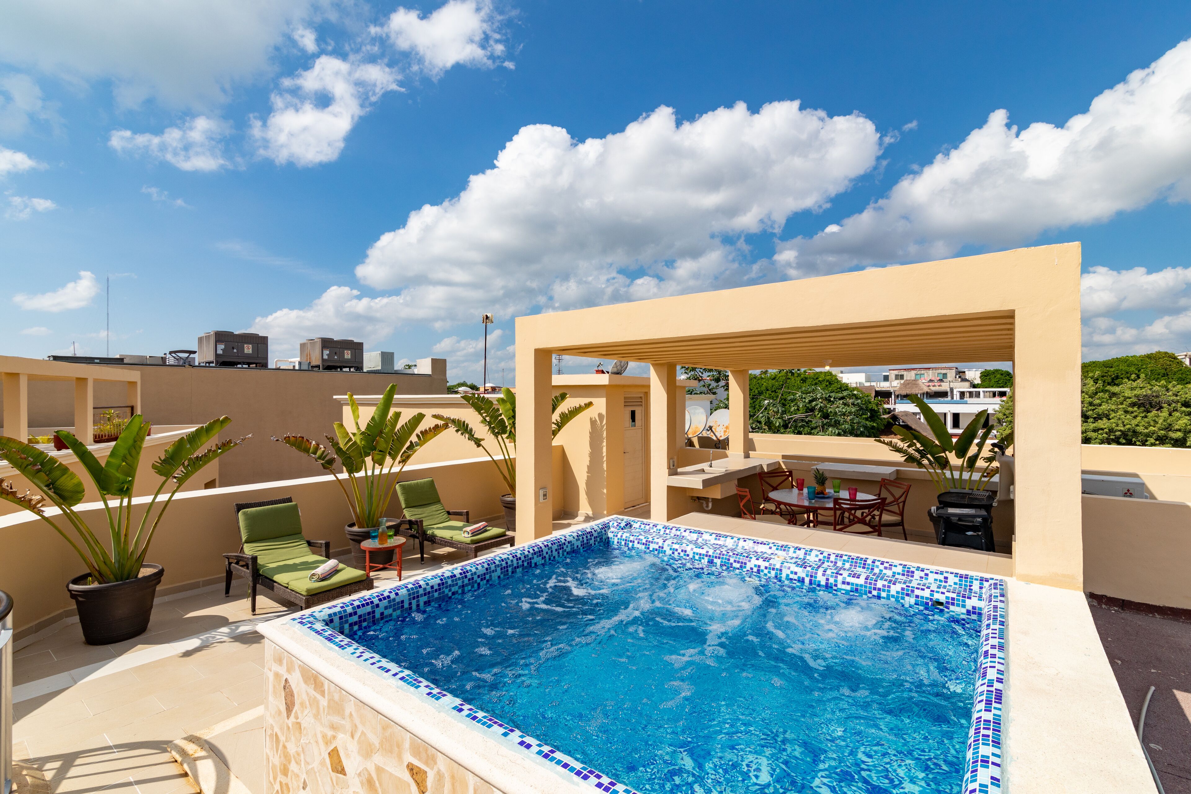 A rooftop pool area with a tiled pool, lounge chairs, and potted plants.
