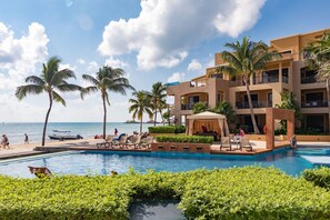 A resort pool area with lounge chairs, palm trees, and a building with balconies.