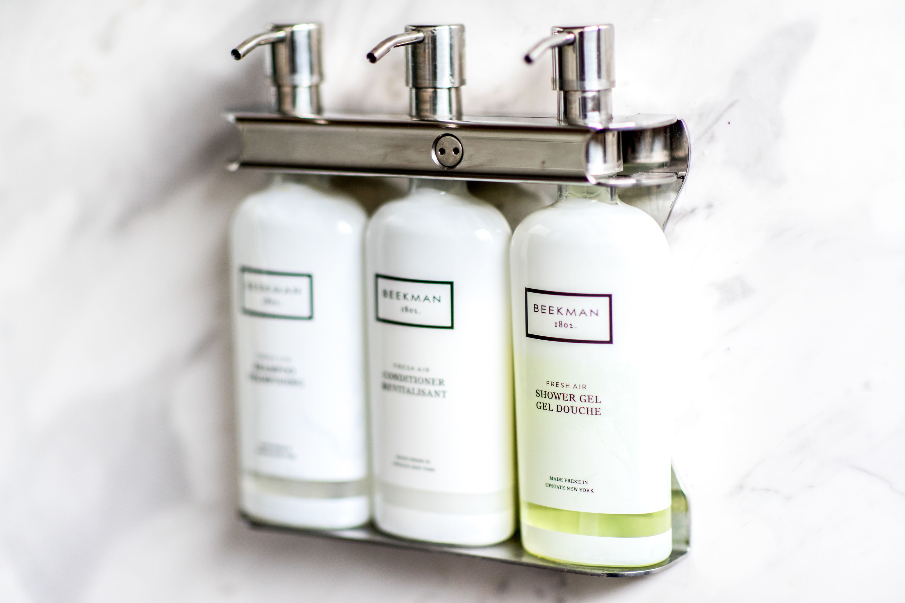 A bathroom shelf with three bottles of Beekman shower gel.