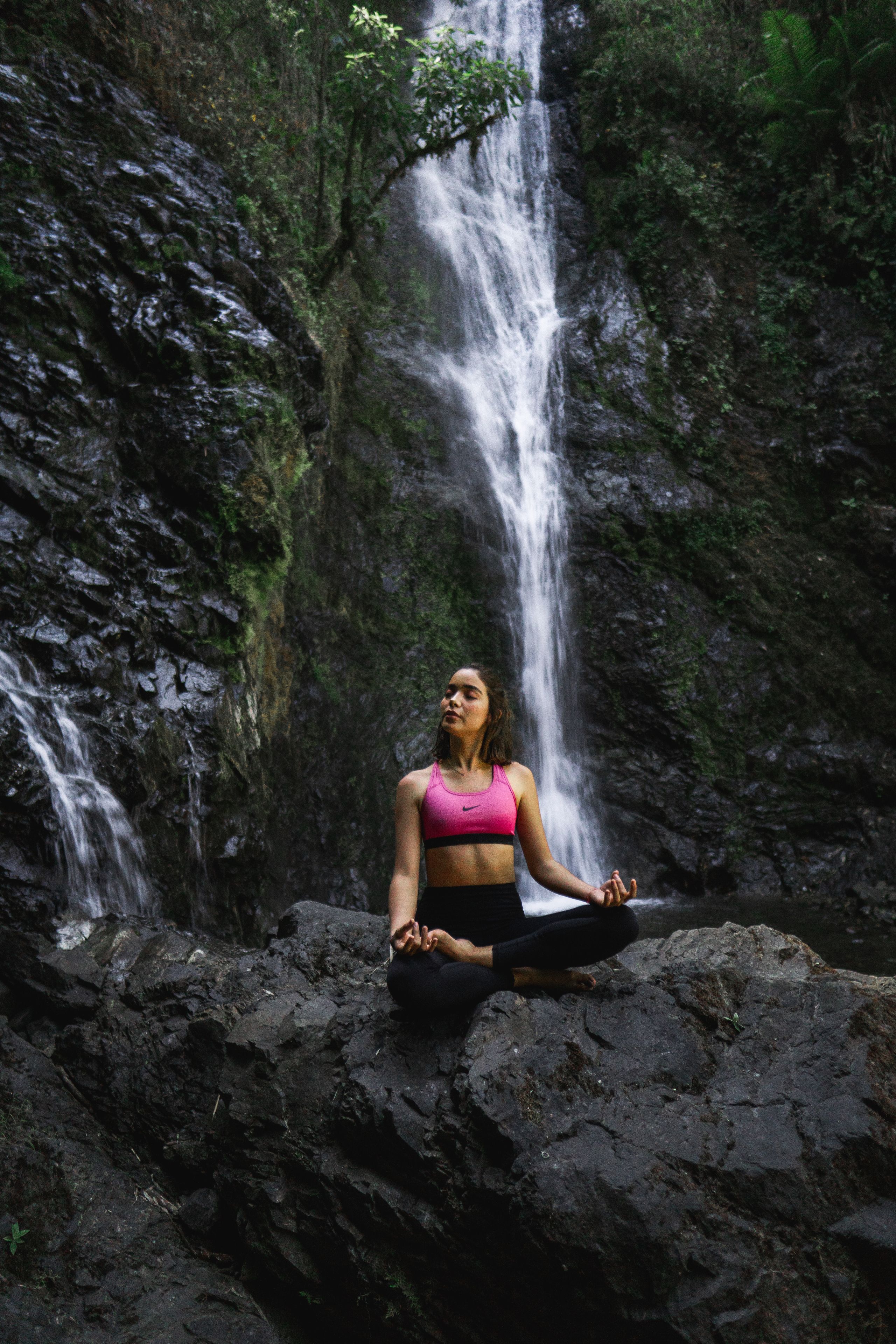 A person meditating on a rock by a waterfall.