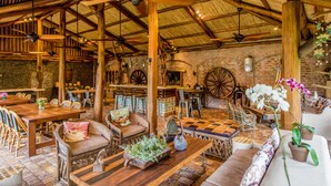 Un interior rústico con mesas y sillas de madera, un muro de ladrillo y una gran rueda de madera.
