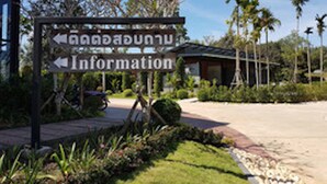 A signpost with directions to 'Information' and a building with a sloped roof, surrounded by greenery and palm trees. - Sangkhlakiri Resort (Sangkhla Buri)