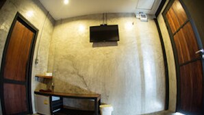 A room with a wooden door, a small desk, a television mounted on the wall, and a trash bin. - Sangkhlakiri Resort (Sangkhla Buri)