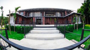 A modern building with a curved facade, a central entrance with steps, and a surrounding green lawn. - Sangkhlakiri Resort (Sangkhla Buri)
