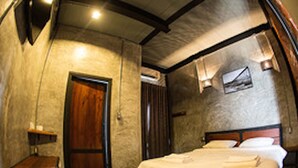 A bedroom with a wooden door, a bed with white linens, a nightstand, and a wall-mounted light fixture. - Sangkhlakiri Resort (Sangkhla Buri)