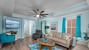 A living room with a TV, a sofa, a coffee table, and a ceiling fan. - BEAUTIFUL 5-BEDROOM HOUSE WITH HEATED SWIMMING POOL, GAS GRILL, LARGE DECK (Galveston)