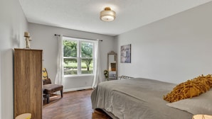 Une chambre à coucher avec un lit, une armoire en bois, une chaise, une fenêtre avec des rideaux et un luminaire au plafond.