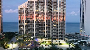 A high-rise hotel with multiple balconies, a parking area, and a view of the ocean.