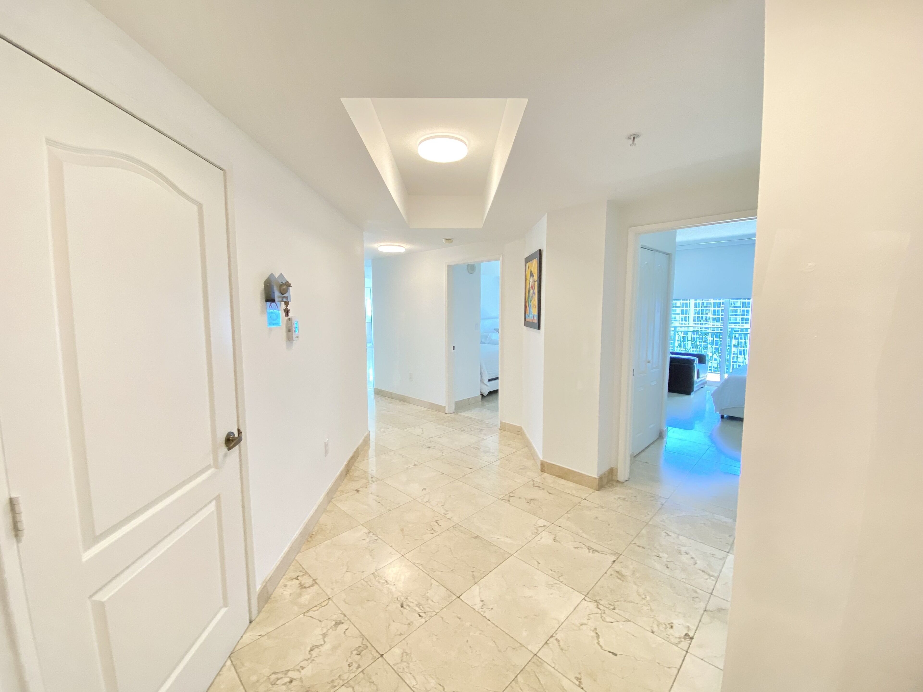 A hallway with a tiled floor, white walls, and a ceiling with recessed lighting.