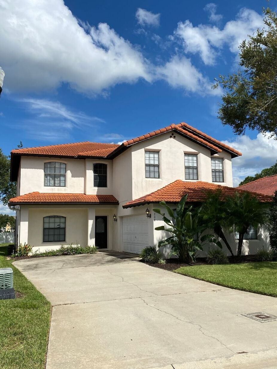 A two-story house with a red-tiled roof, a front entrance, and a driveway leading to the garage.