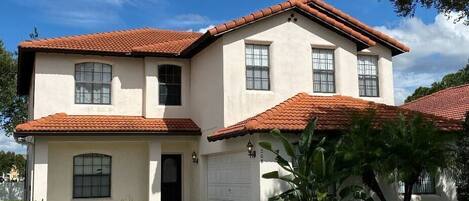 A two-story house with a red-tiled roof, a front entrance, and a driveway leading to the garage.