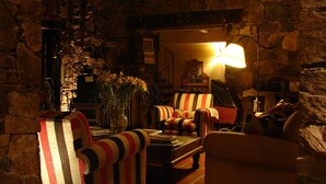 Una habitación acogedora con paredes de piedra, sillones a rayas, una mesa con libros y una lámpara.