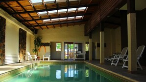 Una piscina interior con agua cristalina, rodeada de sillones de descanso y un muro de piedra.