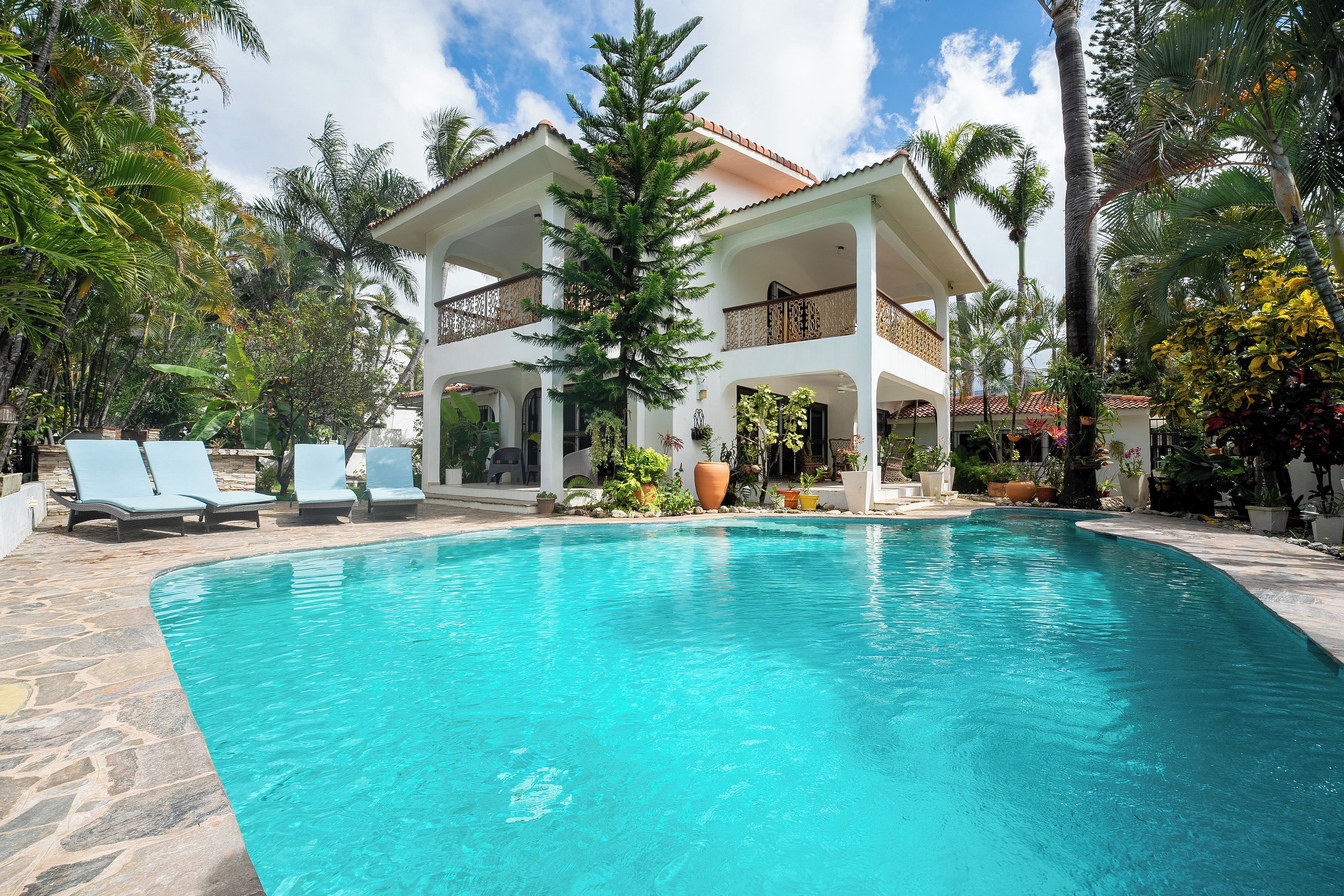 A pool area with lounge chairs, a two-story building, and tropical vegetation.