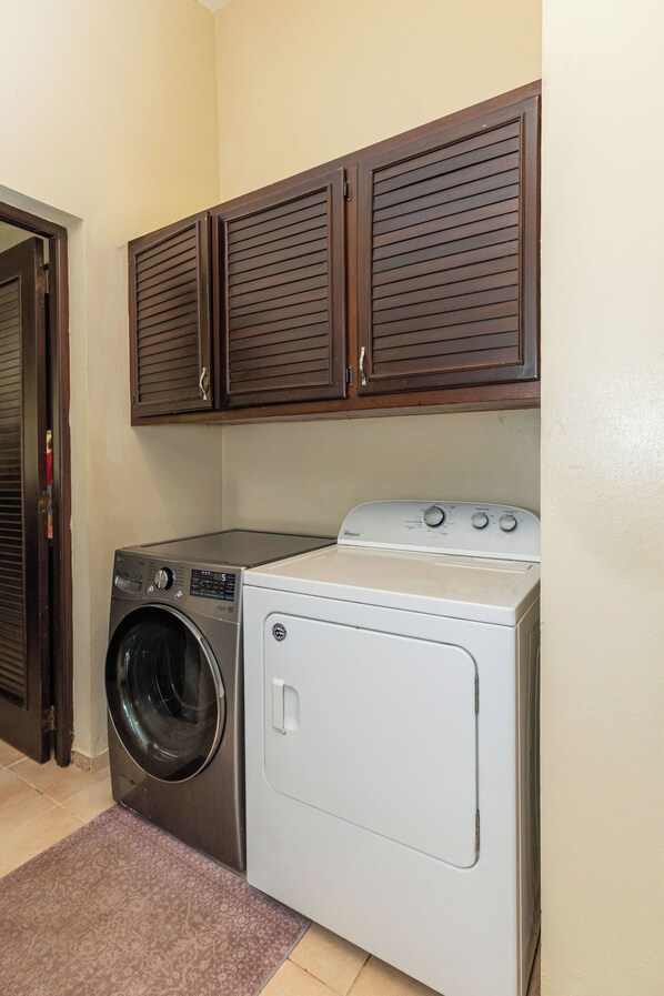 A laundry area with a front-loading washer and dryer, wooden cabinets above, and a patterned rug on the floor.