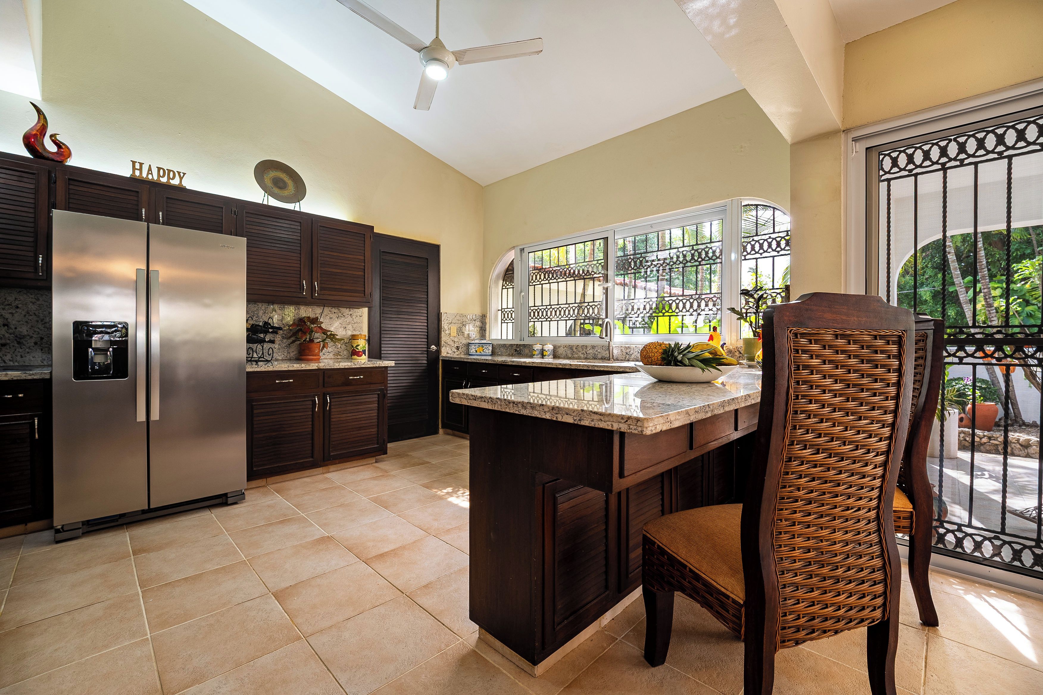 A kitchen with dark cabinetry, a stainless steel refrigerator, a granite countertop, and a wicker chair.