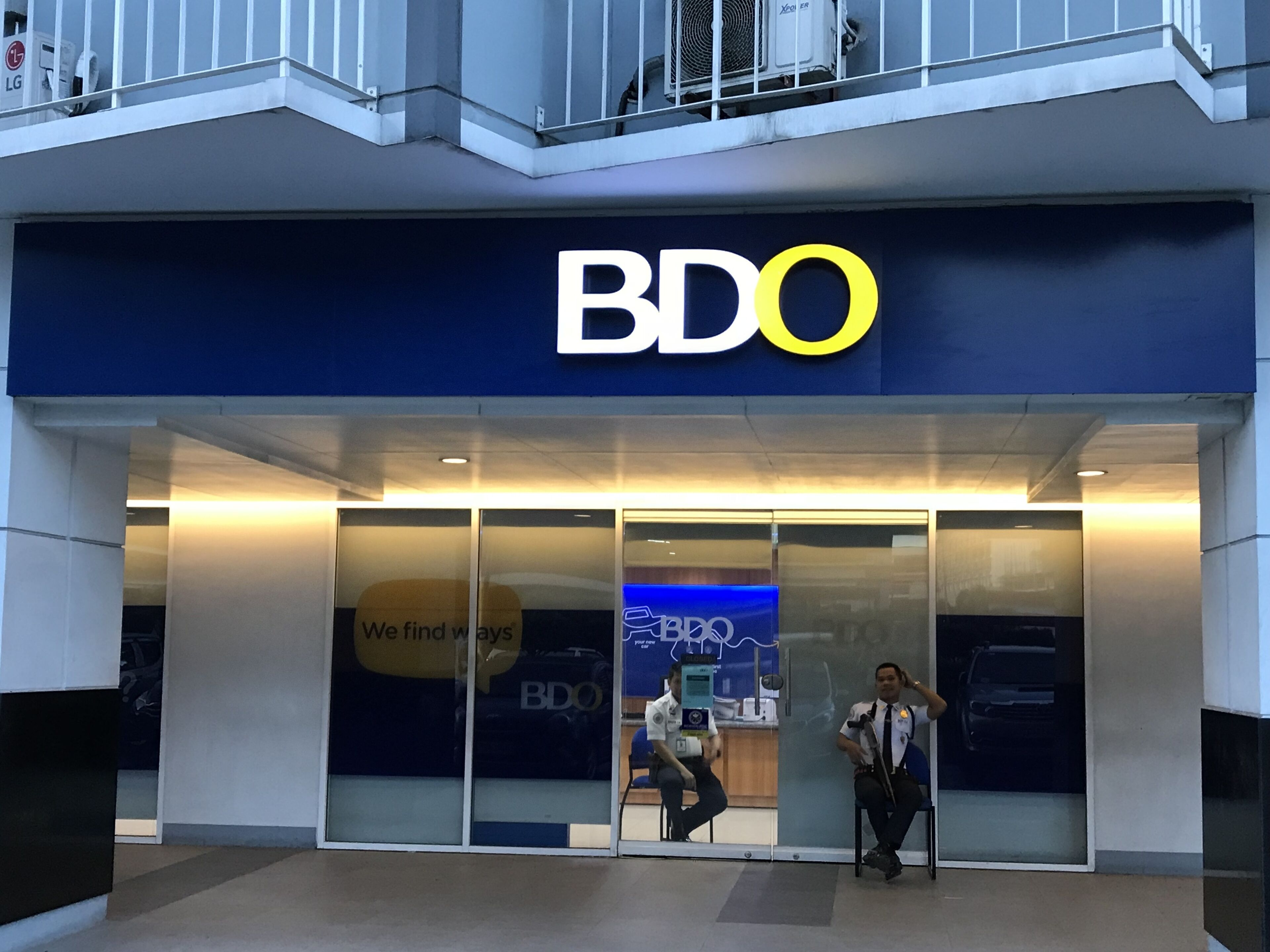 Una tienda BDO con fachada de vidrio y un guardia de seguridad en el exterior.