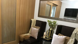 A modern living room with two dark brown sofas, a beige throw blanket, and a small side table with a vase of flowers and a candle. - Best Value 5-Star QCondo across Mall of Asia, near Airport, Casinos & Manila Bay (Pasay)
