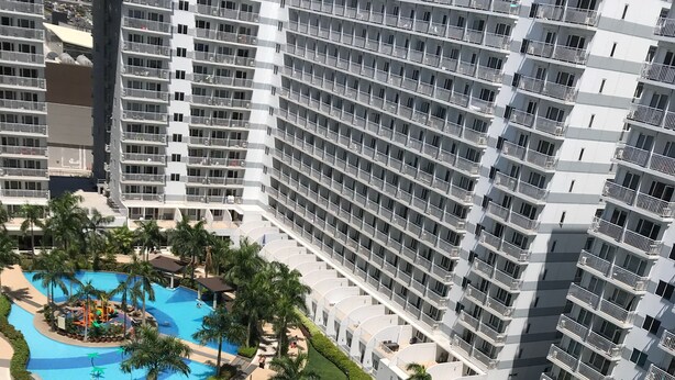 A high-rise hotel with multiple balconies, a central swimming pool, and surrounding greenery. - Best Value 5-Star QCondo across Mall of Asia, near Airport, Casinos & Manila Bay (Pasay)