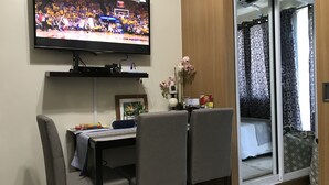 A room with a TV mounted on the wall displaying a sports event, a dining table with chairs, and a sliding glass door leading to a balcony with patterned curtains. - Best Value 5-Star QCondo across Mall of Asia, near Airport, Casinos & Manila Bay (Pasay)