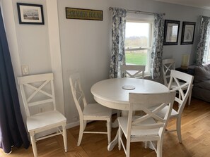 A dining area with a round white table and four white chairs. There is a sign on the wall that reads "PARADISE FOUND". - Ocean View Home With Large Yard, A/c, Hot Tub, Walk To Sandy Beach, Pets Ok (Narragansett)