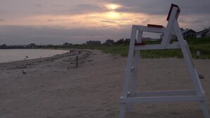 A beach with a white beach chair and a sign in the background. - Ocean View Home With Large Yard, A/c, Hot Tub, Walk To Sandy Beach, Pets Ok (Narragansett)