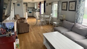 A spacious living room with a white sofa, a dining table with chairs, and a kitchen in the background. - Ocean View Home With Large Yard, A/c, Hot Tub, Walk To Sandy Beach, Pets Ok (Narragansett)