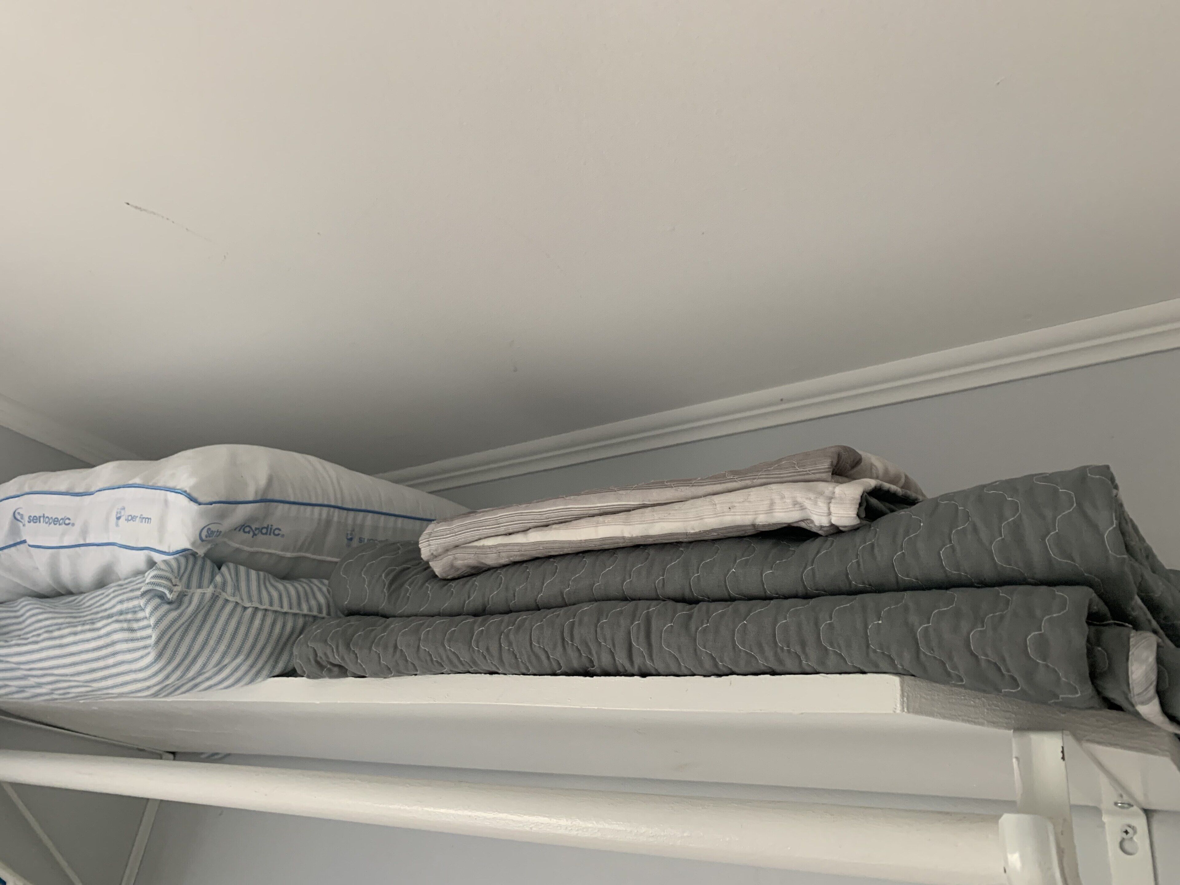 Un lit superposé avec une tête de lit blanche et un matelas agrémenté d’un oreiller à rayures.