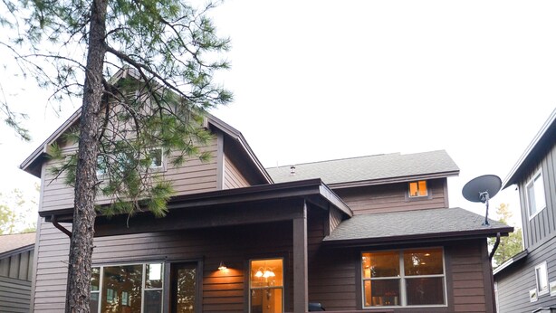 A two-story house with a wooden deck, a satellite dish, and a stone pathway leading to the front door.