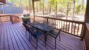 A covered outdoor deck with a grill, table, and chairs.