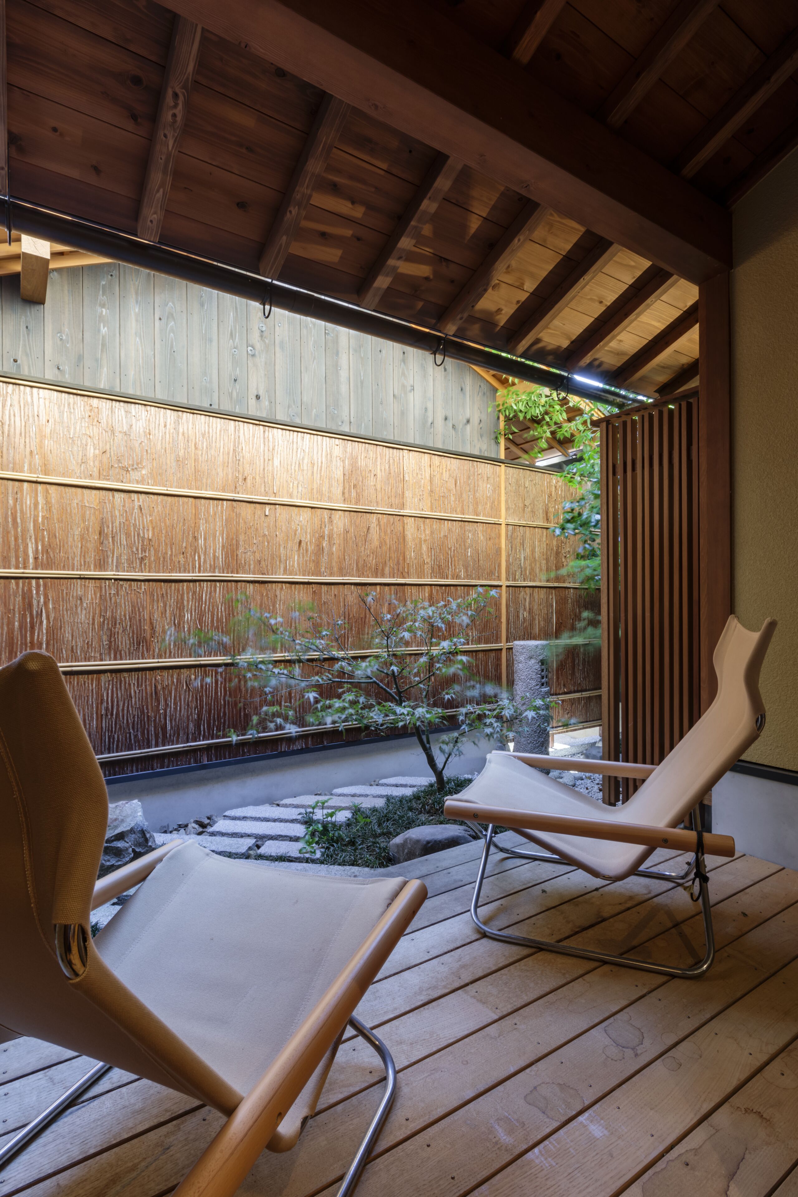 A wooden deck with two lounge chairs and a bamboo fence.