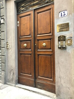A wooden double door with a brass handle, a number plate indicating the address, and a plaque with text.