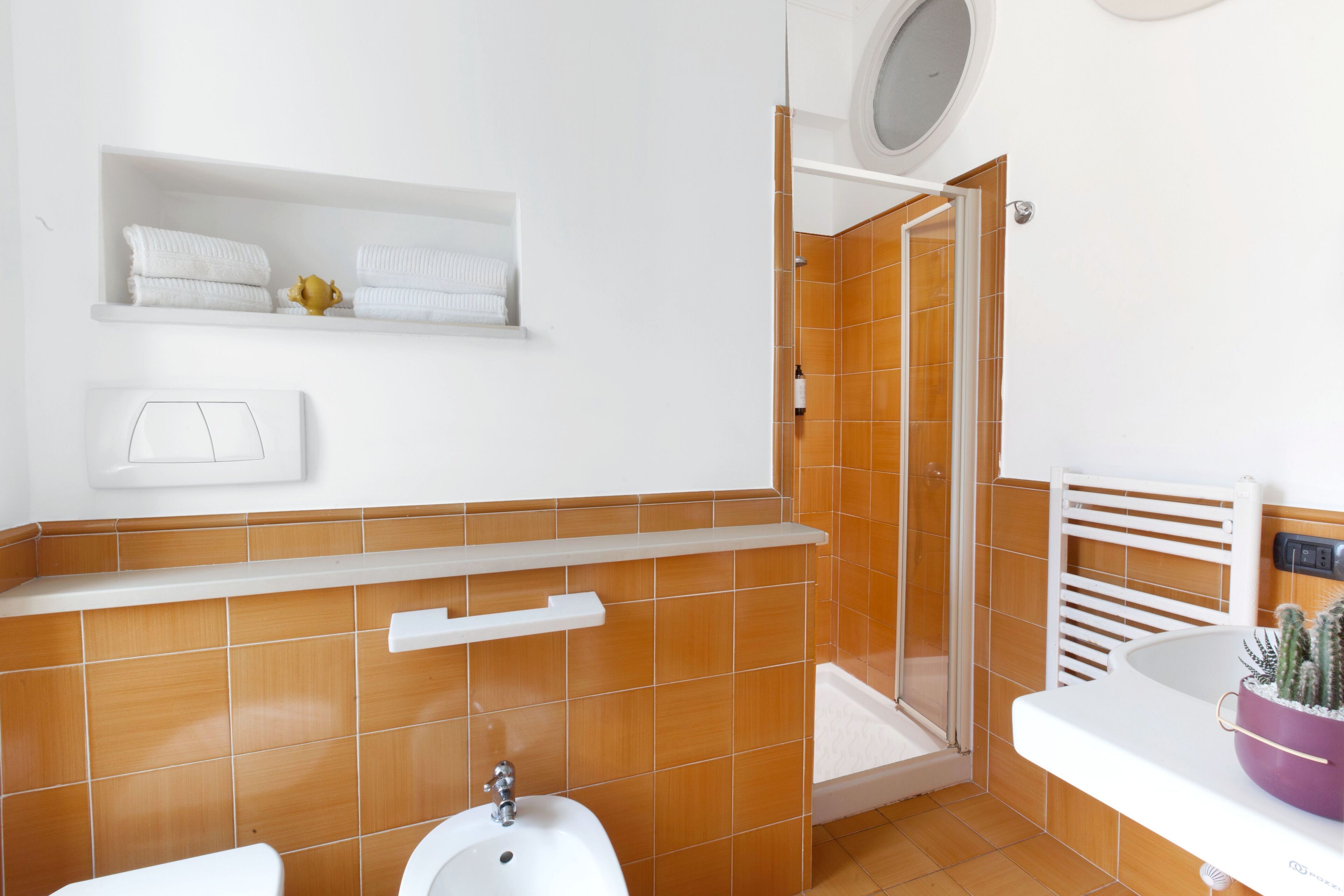 Un baño con un lavamanos blanco, un inodoro, una ducha con puerta de cristal y un estante con toallas.