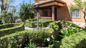 Una casa con fachada de ladrillo, un balcón con barandilla y un jardín cuidado con setos y plantas.