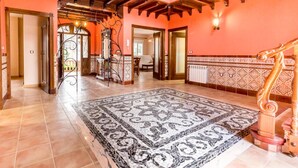Un pasillo amplio con alfombra estampada, vigas de madera en el techo y una escalera con barandillas decoradas.