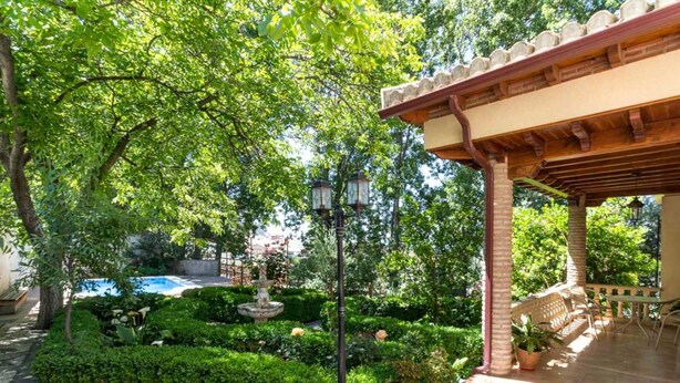 Un jardín con una fuente, una pérgola y una piscina.