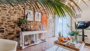 Un salon chaleureux avec un mur en pierre, une console blanche, un canapé confortable et un téléviseur.