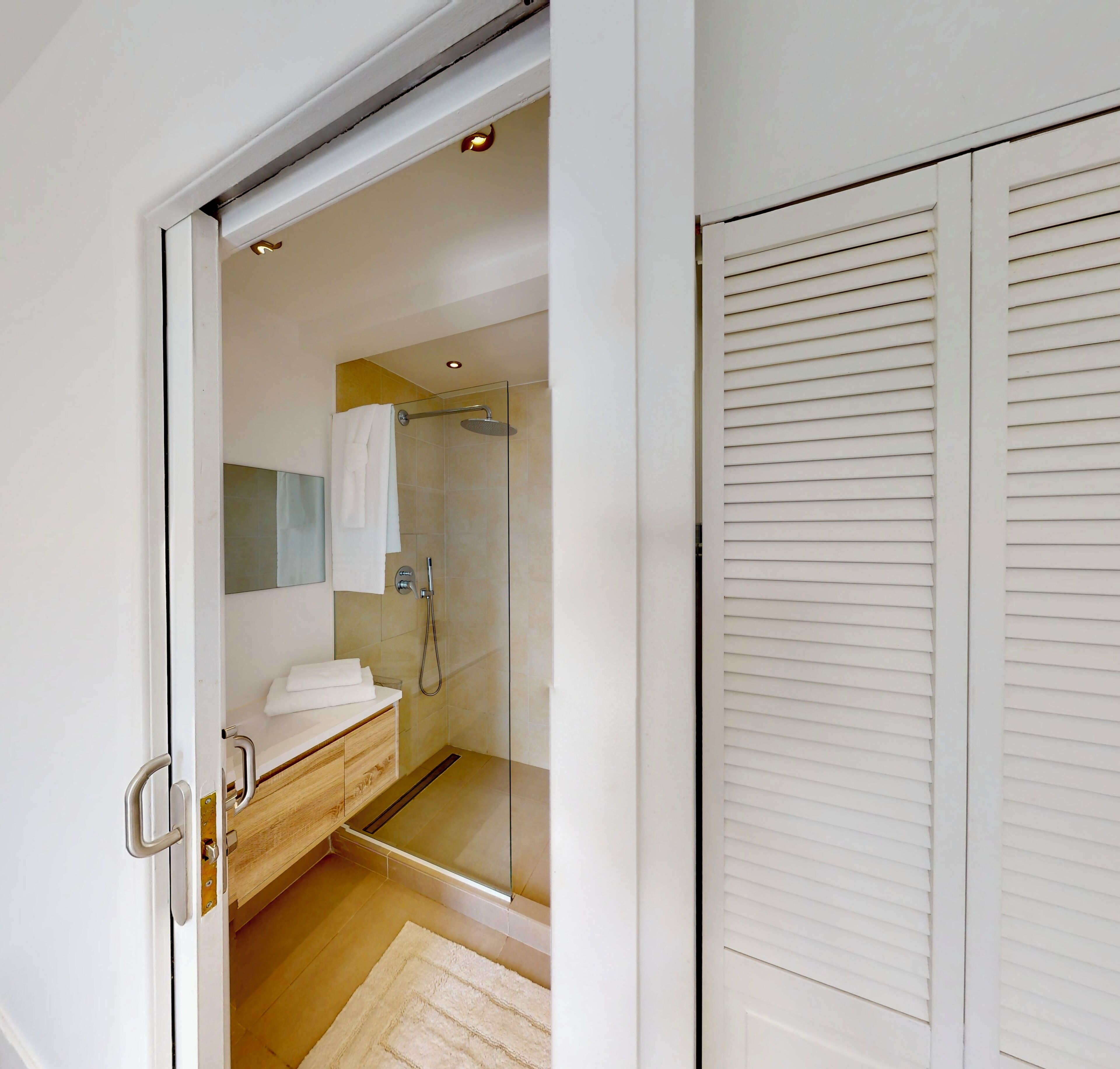 Un baño moderno con cabina de ducha de vidrio, tocador de madera y una toalla blanca sobre el mostrador.