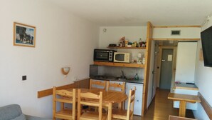 A compact living space with a kitchenette, a dining area with wooden furniture, a small refrigerator, and a single wall-mounted television. - Arc 2000, studio direct access to  tracks, South balcony (Bourg-Saint-Maurice)
