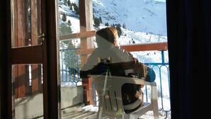 A person sitting on a chair by a window overlooking a snowy mountain landscape. - Arc 2000, studio direct access to  tracks, South balcony (Bourg-Saint-Maurice)