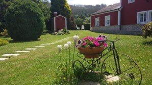 Un jardín con un sendero que lleva a un edificio rojo, una silla de metal y una maceta.