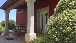 Un espacio de estar al aire libre cubierto, con mesa y sillas, una puerta y un seto bien cuidado.