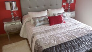 Una cama bien hecha con cabecera gris, dos mesitas de noche con lámparas y una pared roja.