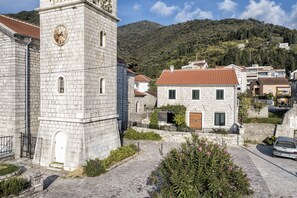 Una chiesa in pietra con una torre campanaria, circondata da edifici residenziali con tetti in tegole rosse.