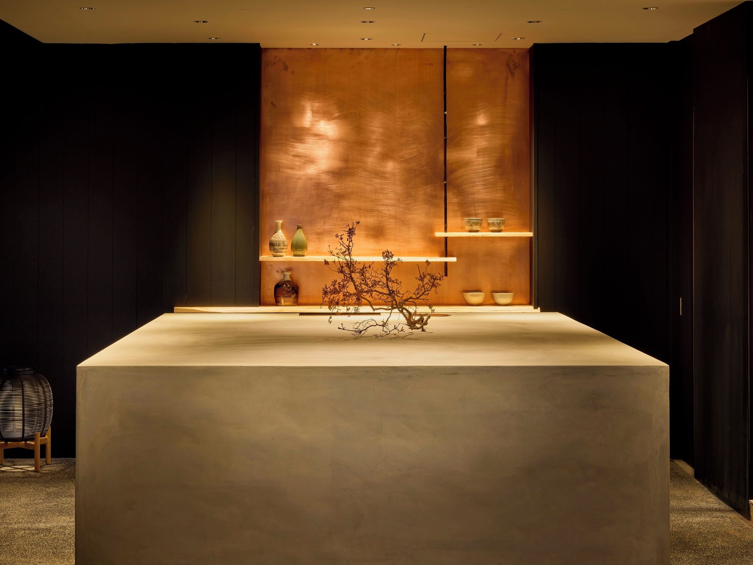 Un área de recepción moderna y minimalista, con un mostrador central, estanterías con objetos decorativos y una pared de tonos oscuros.