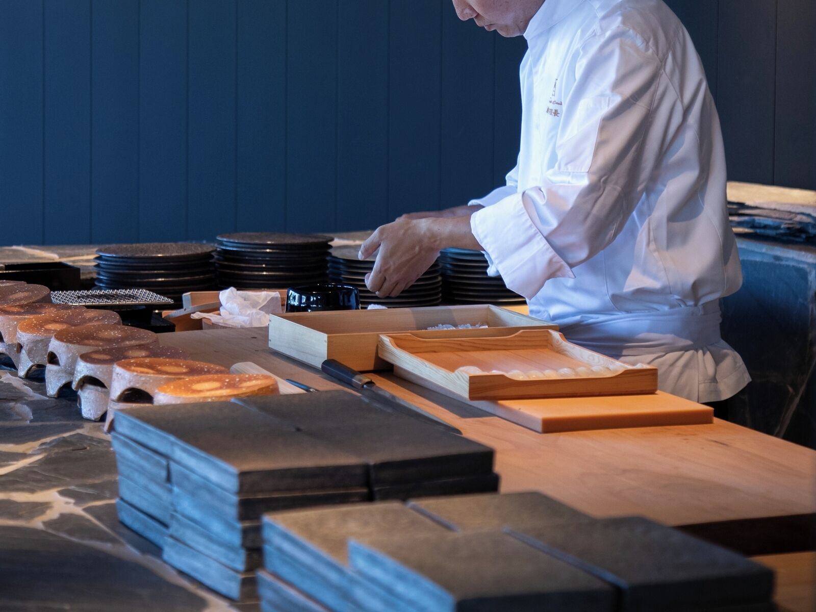 A chef in a white uniform preparing food at a wooden table with various kitchen tools and ingredients.