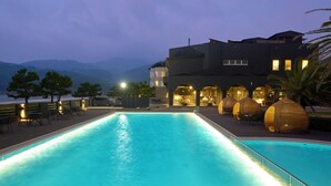 A swimming pool with a view of mountains, a building with multiple balconies, and outdoor seating areas. - ONCRI-KARATSU (Karatsu)