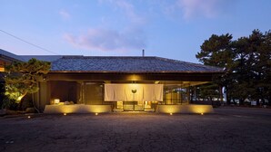 A traditional Japanese house with a tiled roof, a wooden exterior, and a small garden area with a tree and a bench. - ONCRI-KARATSU (Karatsu)